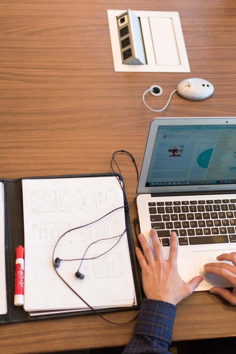 Overhead view of a person working remotely with a laptop and documents on a wooden desk.